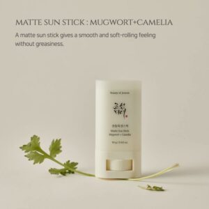 Skønheden ved Joseon Matte Sun Stick: Bygnurt + Kamelia (18 g) står oprejst på en lys beige overflade med grønt, mens teksten ovenfor fremhæver den glatte, ikke-fedtende påføring.