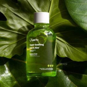 En grøn flaske Jumiso - Super Soothing Cica & Aloe Essence Toner 125ml hviler på et stort blad i naturligt sollys og fremviser den klare væske og den synlige forsideetiket.