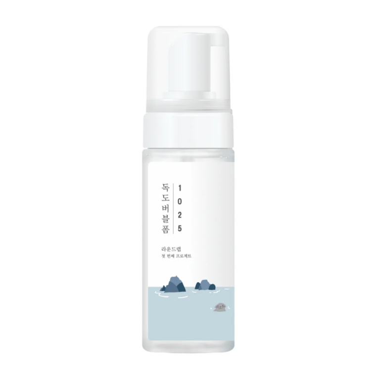 En klar plastikpumpeflaske med en hvid låg har koreansk tekst og en illustration af klippeøer og en skildpadde på etiketten, der fremhæver Round Lab - 1025 Dokdo Bubble Foam Cleanser (150 ml) med et minimalistisk design.