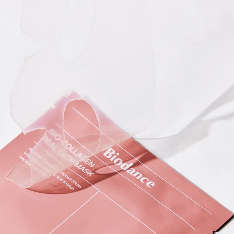 En gennemsigtig gel-ansigtsmaske tages ud af en pink, rektangulær Biodance-pakke med Header Template-designet og produktnavnet Bio-Collagen Real Deep Mask, som er tydeligt på emballagen.