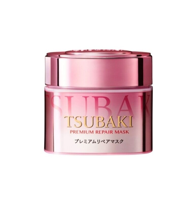 En skinnende, reflekterende lyserød og gylden krukke mærket "Shiseido - Tsubaki Premium Repair Mask Pink Camellia 180g" med japansk tekst og et matchende lyserødt låg er placeret mod en almindelig hvid baggrund.