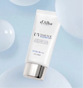 En hvid tube med d'Alba - UV Essence Waterfull+ Sun Cream SPF50+ PA++++ hviler på en lyseblå overflade med gennemskinnelige bobler i baggrunden.