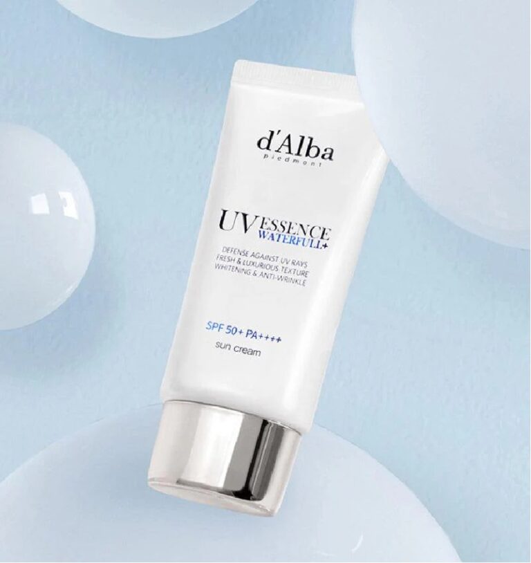 En hvid tube med d'Alba - UV Essence Waterfull+ Sun Cream SPF50+ PA++++ hviler på en lyseblå overflade med gennemskinnelige bobler i baggrunden.