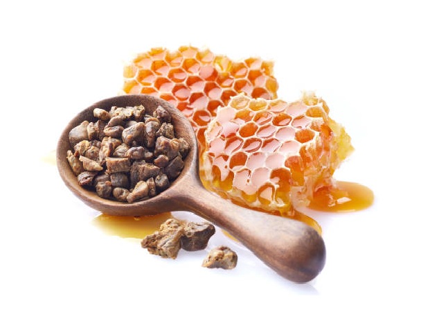 En træske fyldt med propolisstykker hviler ved siden af to stykker honningkage, der drypper med gylden honning på en hvid baggrund, og fremhæver naturens sødme for ethvert ingrediensleksikon.