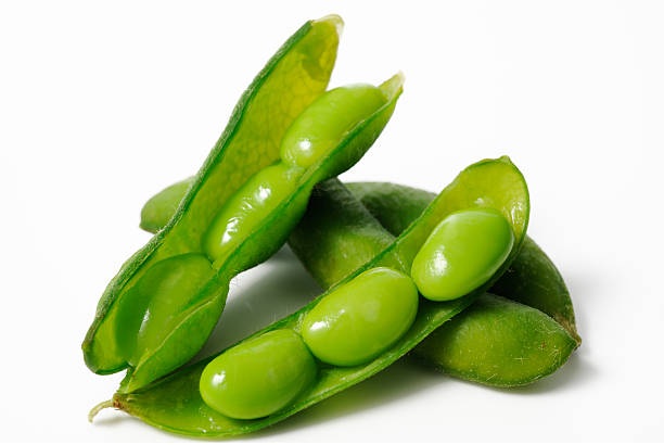 Nærbillede af friske grønne edamamebælge, hvoraf nogle er åbne og afslører skinnende grønne bønner indeni, arrangeret på en hvid baggrund - en perfekt tilføjelse til ethvert ingrediensleksikon.