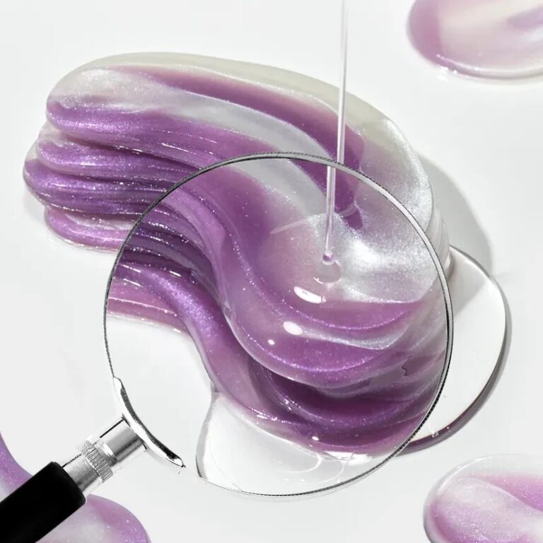 Et forstørrelsesglas svæver over en hvirvel af skinnende lilla og hvid gel med en dråbetæller, der doserer klar væske på den og fremhæver gelens skinnende struktur.
