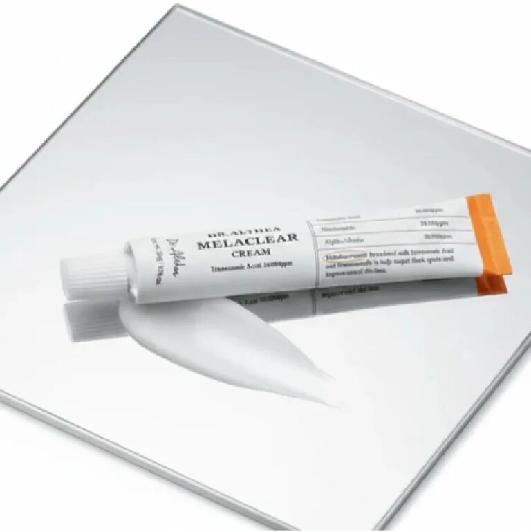 Dr. Althea - Melaclear Cream, der har en livlig orange hætte og er kendt for at lysne huden, hviler på en reflekterende overflade med en klat af den hvide creme presset ud ved siden af tuben.