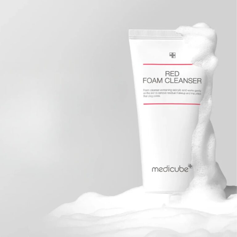 En hvid tube med Medicube - Red Foam Cleanser står oprejst med skum i bunden og på siden mod en lysegrå baggrund. Emballagen har en ren rød og sort tekst, som giver et enkelt og moderne look.