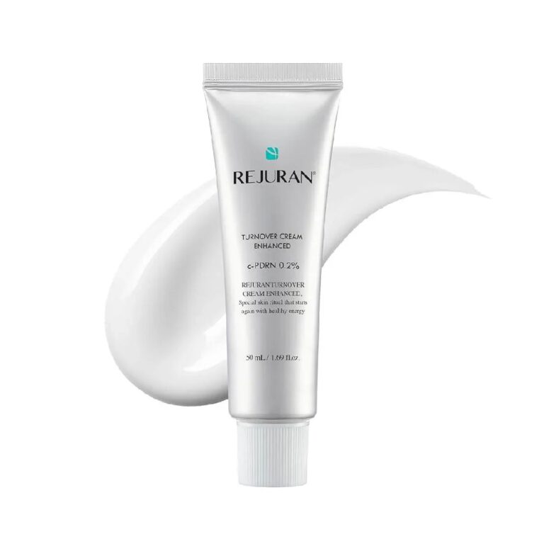 En tube Rejuran – Turnover Cream Enhanced står oprejst på en baggrund af hvid creme, hvor den elegante hvid- og sølvfarvede design med det grønne Rejuran-logo træder tydeligt frem og fremhæver den avancerede formel i denne fornyende creme.