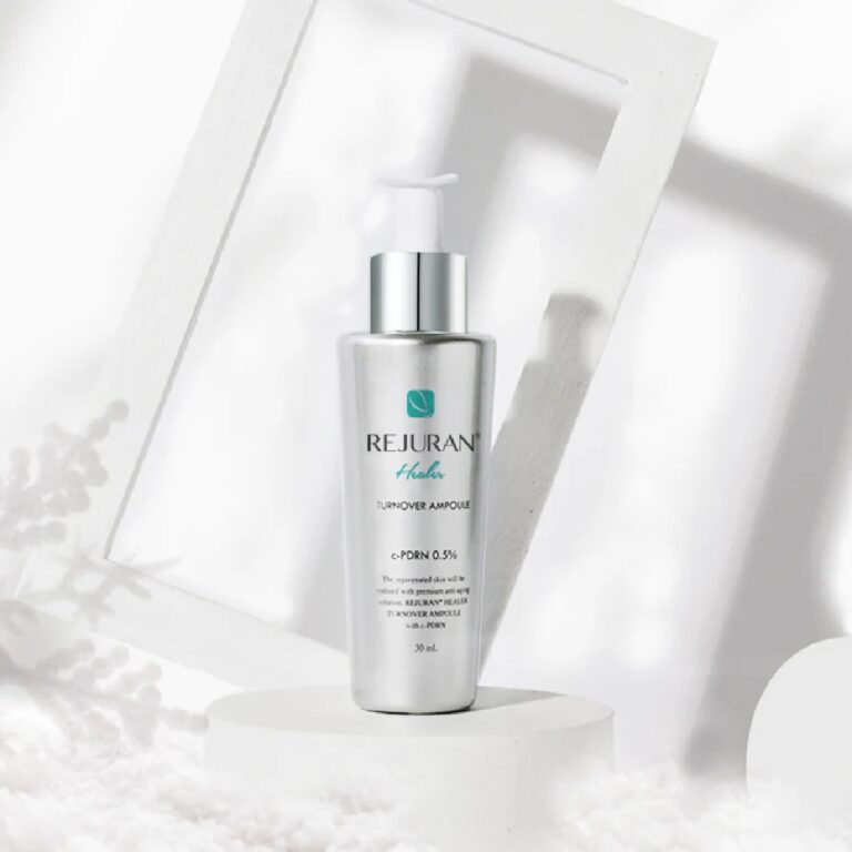 Rejuran – Turnover Ampoule, der kommer i en elegant sølvfarvet flaske med pumpedispenser, står på en hvid, rund base omgivet af minimalistiske hvide geometriske former og bløde skygger, hvilket giver et moderne, rent udtryk.