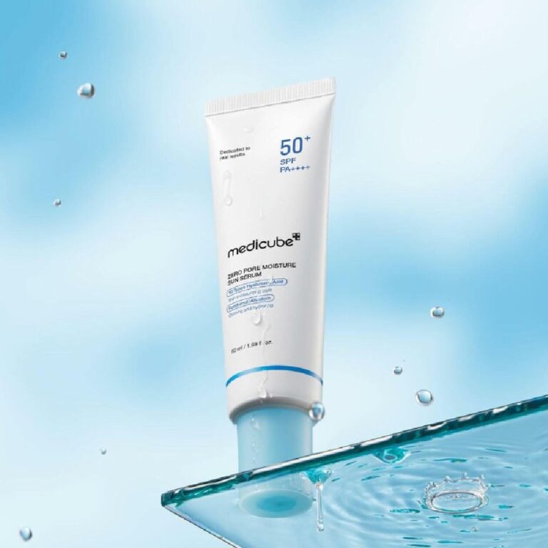 En tube Medicube - Zero Pore Moisture Sun Serum SPF 50+ står oprejst på en glasplade med vanddråber på en lyseblå baggrund med vandsprøjt og flydende dråber for at fremhæve den fugtgivende solbeskyttelse.