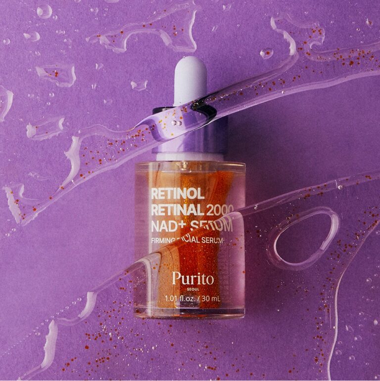 En dråbeflaske med Purito Seoul – Retinol Retinal 2000 NAD+ Serum står på en lilla baggrund, omgivet af en klar væske med guldglimmer og bølgende striber, hvilket fremhæver den kraftfulde kombination af retinol- og retinal-serum, beriget med foryngende NAD+.