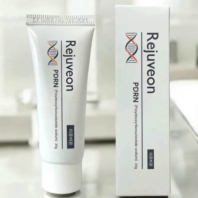 En hvid tube og en æske med Rejuveon – PDRN Cream, med et motiv af en DNA-helix og koreansk tekst, er udstillet på en ren, lys overflade.